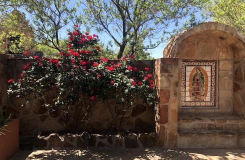 Small stone brick grotto next to large red rose bushes