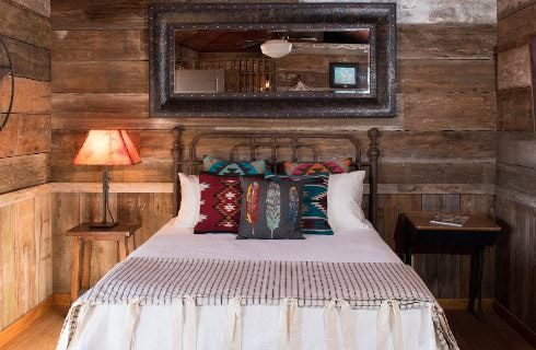 Bedroom with antiqued barn wood paneling on the walls, hardwood flooring, wrought iron bed, white bedding, and large mirror above bed