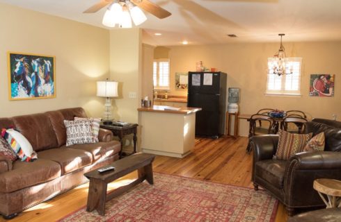 Large room with yellow walls, hardwood flooring, brown leather couch and chair, dining area, and kitchen