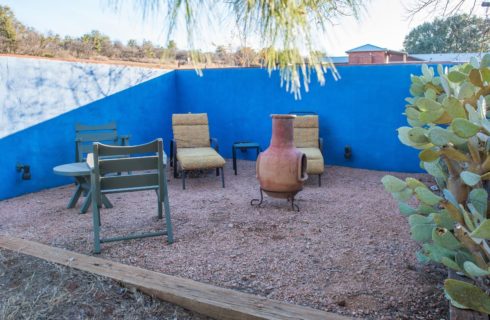 Large enclosed gravel patio with table, chairs, lounge chairs, chiminea, and cactus