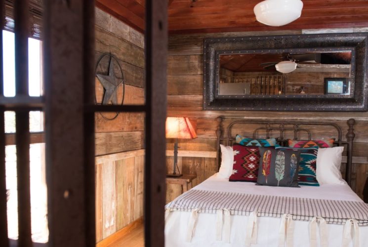 Bedroom that looks like a jail cell with antiqued barn wood paneling on the walls, hardwood flooring, wrought iron bed, and white bedding