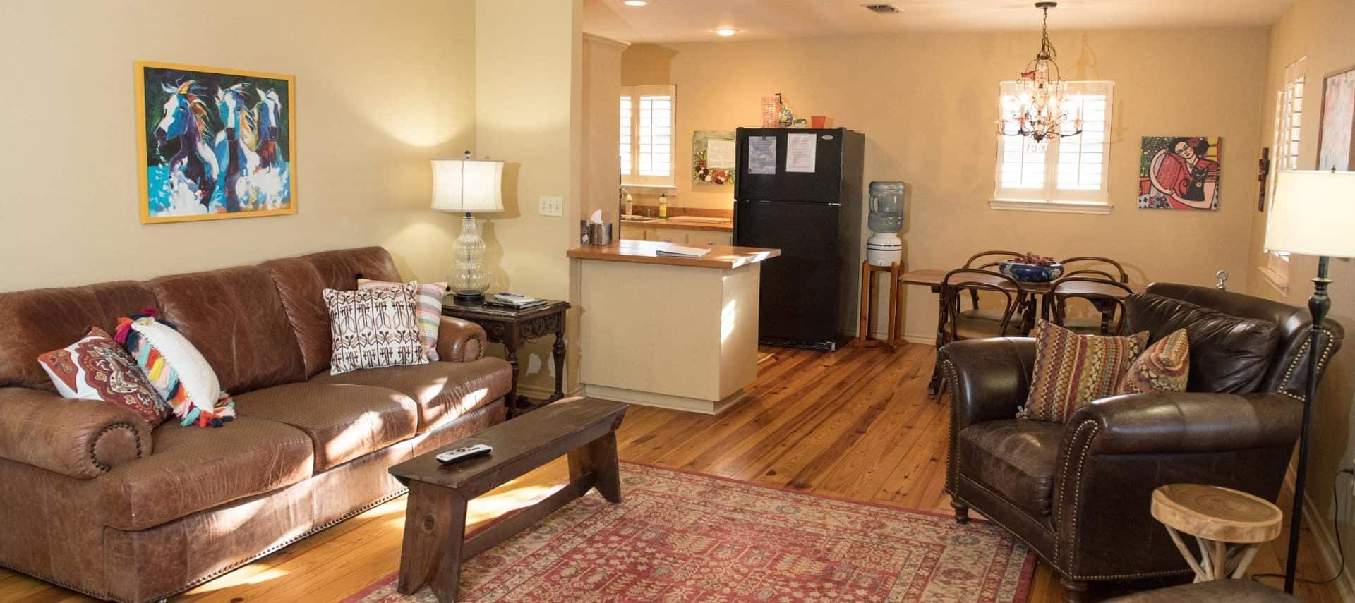 Large room with yellow walls, hardwood flooring, brown leather couch and chair, dining area, and kitchen