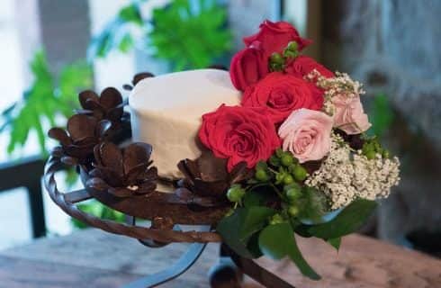 Close up view of small white round cake sitting in wrought iron stand with red and pink roses