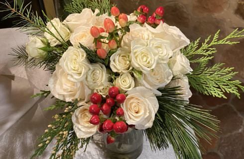 Close up view of flower bouquet of white roses and evergreen sprigs in glass vase